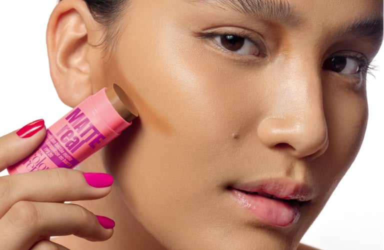 Cinco bases em bastão para pele oleosa da linha "Matte Real Color Trend" da Avon estão organizadas em uma fileira diagonal. Cada bastão está destampado, revelando o topo do produto em diferentes tonalidades, que vão do bege bem claro ao marrom escuro.