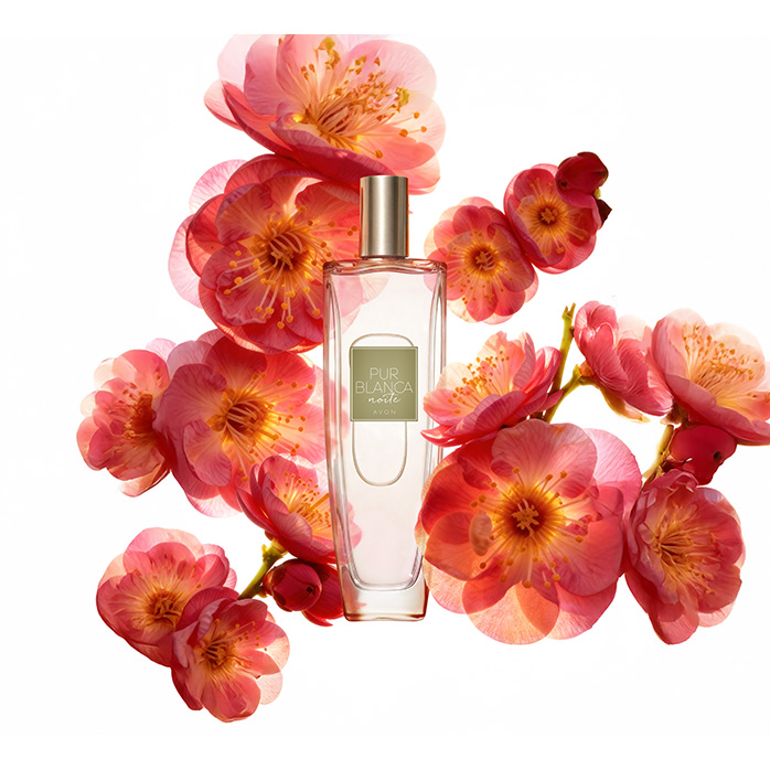 Frasco da fragrância Pur Blanca Noite, rodeada de flores avermelhadas, em fundo branco.