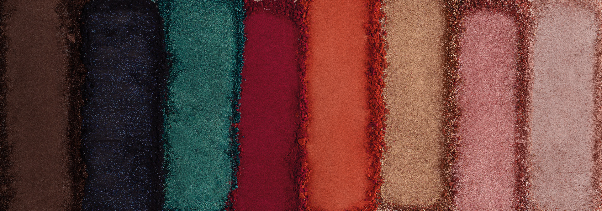 Banner com fundo bege claro. Elementos incluem lápis delineadores Avon em tons vibrantes de rosa e roxo, com traços desenhados ao redor. Texto: "Olhos: mais presentes, mais emoção."