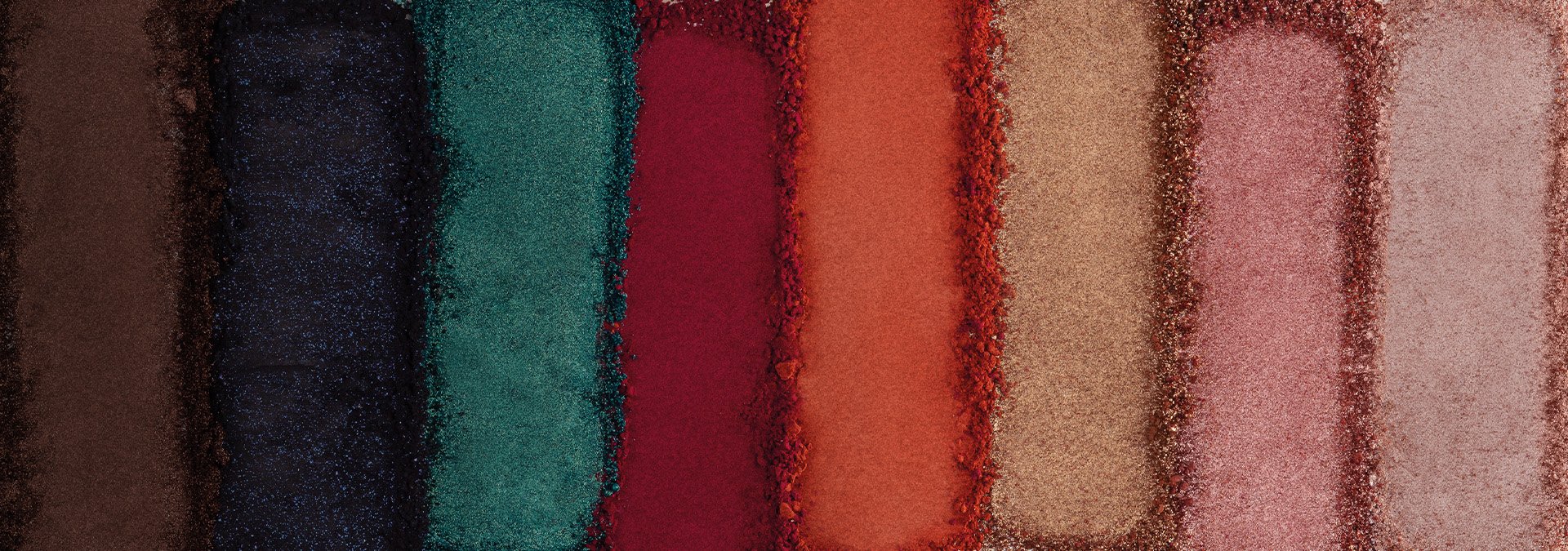 Banner com fundo bege claro. Elementos incluem lápis delineadores Avon em tons vibrantes de rosa e roxo, com traços desenhados ao redor. Texto: "Olhos: mais presentes, mais emoção."