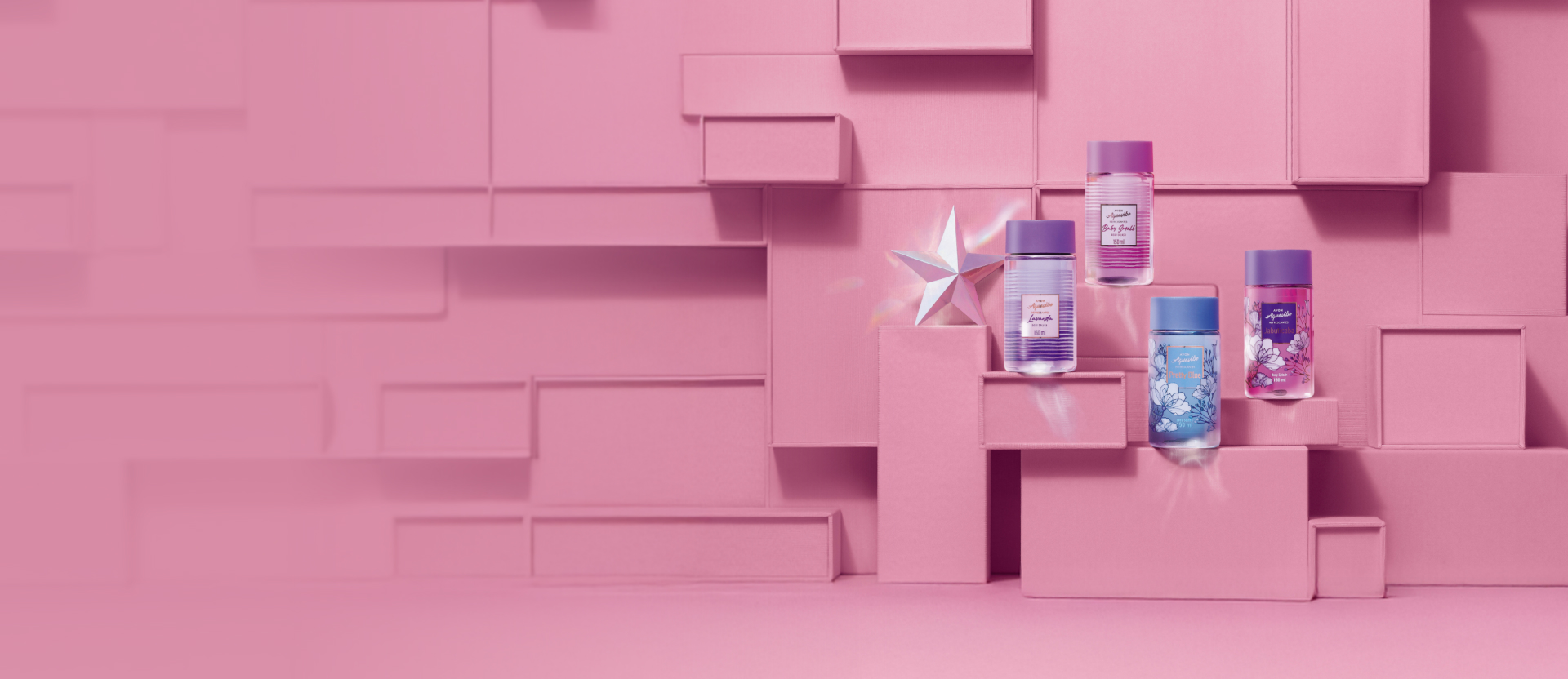 Frascos de Aquavibe Body Splash: Lavanda em lilás, Baby Smell em rosa, Pretty Blue em azul e Jabuticaba em roxo, com estrela prata à esquerda, sobre caixas rosas que compõem o fundo.