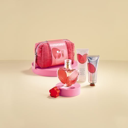 Kit Lov|u com nécessaire rosa, fragrância em frasco de coração e bisnagas de Loção Perfumada para o Corpo e de Creme para as Mãos. Os itens estão sobre plataformas rosa. Fundo bege.