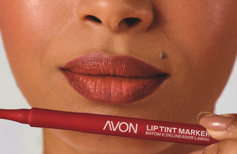 Close-up de lábios com um lip combo marrom e vermelho, utilizando o Lip Tint Vinho da Avon, destacando a aplicação precisa e o efeito de cor natural.