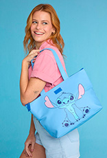 Mulher de cabelos ruivos veste camiseta rosa e short azul e segura bolsa da coleção Stitch em fundo azul.