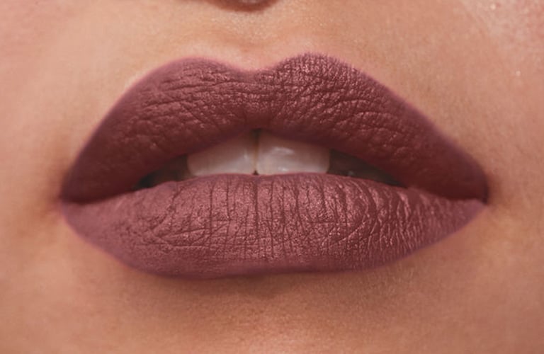 Foco em lábios com batom que não sai da boca na cor nude marrom de Power Stay da Avon. A modelo tem um piercing de argola no nariz e no septo.