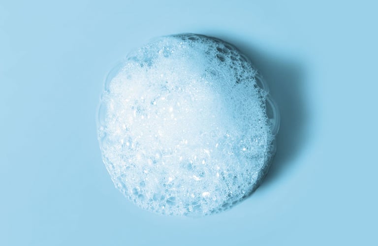 Espuma de limpeza na cor branca posicionada no centro sobre um fundo azul-claro liso e sólido.