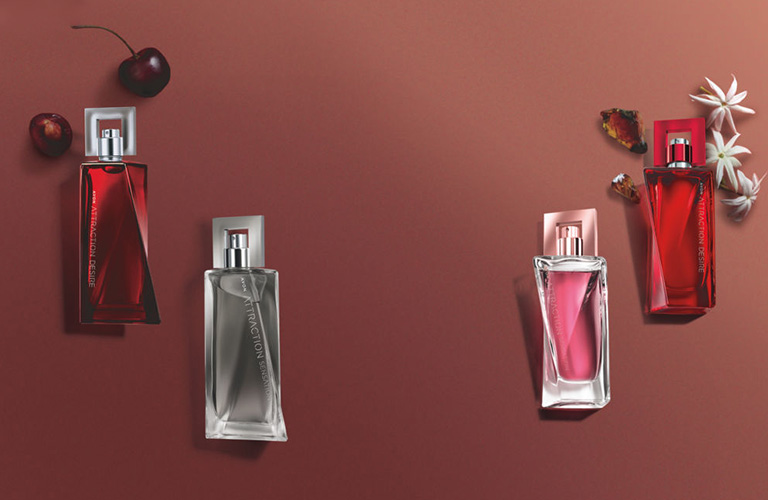 Quatro tipos de perfume da linha Attraction Avon nas cores vermelho, cinza e rosa em um fundo marrom neutro.