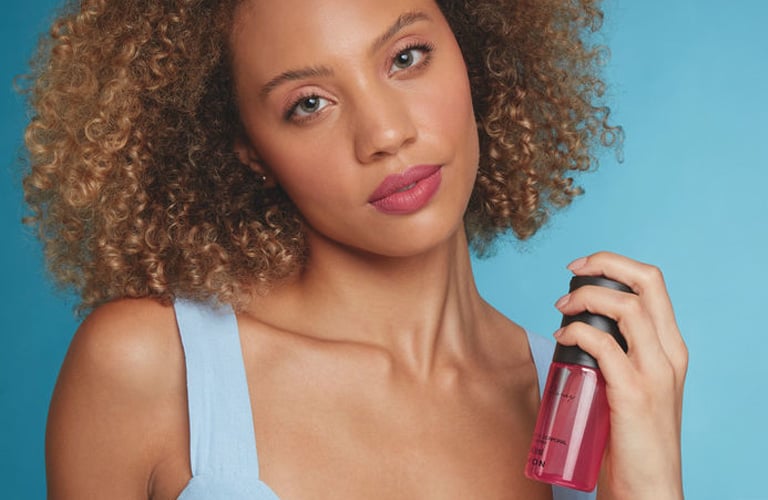 Modelo com cabelos cacheados e blusa lilás de alças segura frasco de Desodorante Spray Far Away para mulheres.