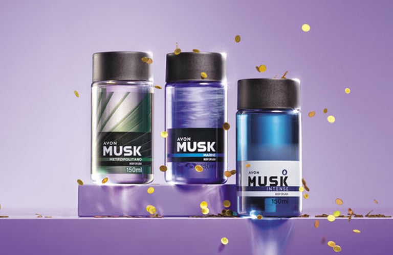 Três frascos de body splash masculino Musk sobre fundo lilás com partículas douradas brilhantes.