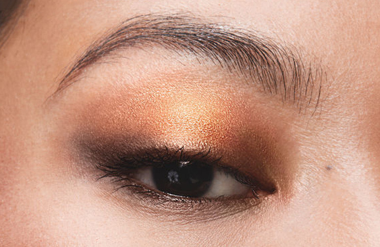 Close-up de rosto com maquiagem marrom com dourado nos olhos e batom escuro, realçando o efeito da Paleta Quarteto Bronze da Avon.