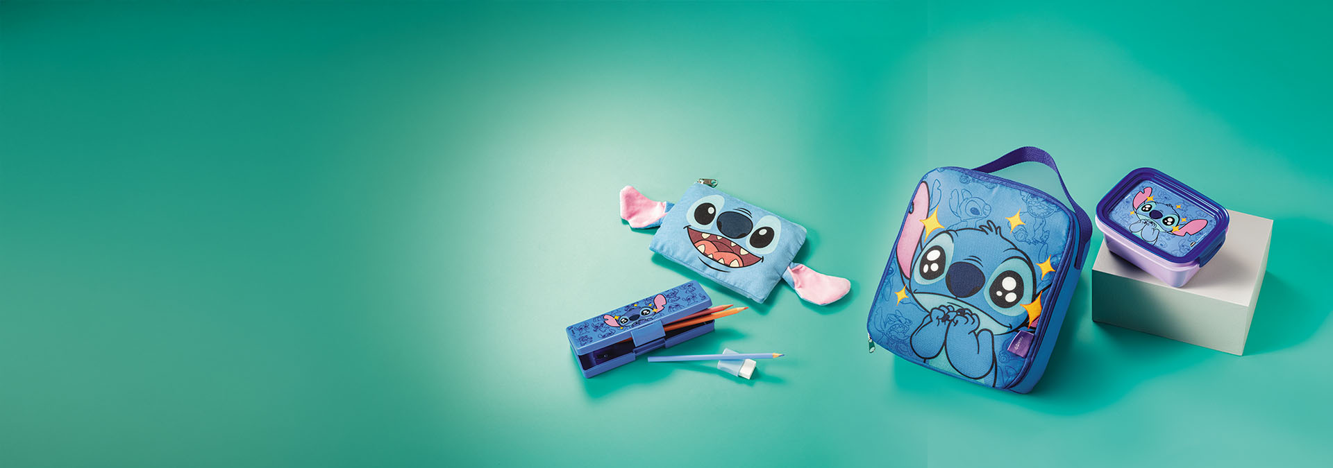 Banner com produtos infantis sobre fundo verde. Inclui lancheira, estojo e necessaire com estampas do personagem Stitch. Texto: "Estimule a imaginação dos pequenos com nossos produtos divertidos!"