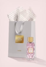 Frasco em vidro facetado e tampa dourada de Charisma Magnetic à frente de sacola de presente cinza com texto Iconic Collection Avon, e papel de seda branco. Fundo claro.