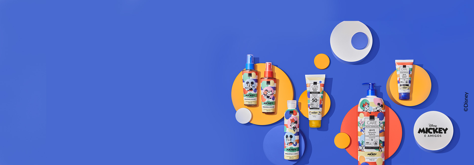 Itens da coleção Disney Mickey e Amigos: Colônias Mickey e Minnie, Shampoo e Condicionador 2 em 1, Protetor Solar, Loção Corporal e Creme para as Mãos, sobre círculos de diversas cores, em fundo azul.