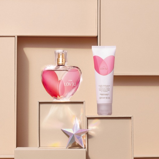 Frasco em tons de rosa com formato de coração de Deo Parfum LOV|U e bisnaga branca com rosa de Loção Corporal LOV|U, com estrela prata, sobre caixas beges, que compõem o fundo.