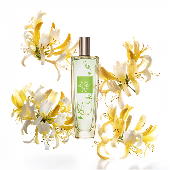 Frasco da fragrância Pur Blanca Hope, rodeada de flores amareladas, em fundo branco.