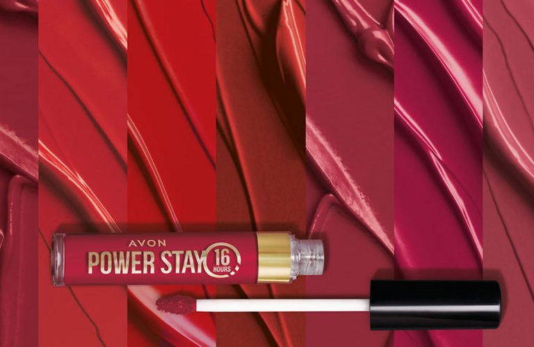 Batom que não sai da boca líquido de Power Stay da Avon no tom vermelho e disposto em um fundo com texturas vermelhas e vinho.