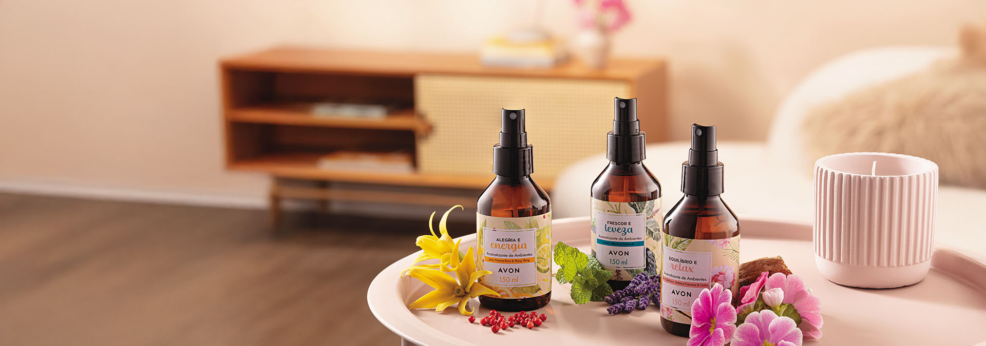 Banner em fundo claro, três frascos de perfumação para ambientes e uma vela em um suporte rosa, acompanhados de flores coloridas. Texto: "Sinta a leveza dos aromas e renove a energia do seu lar."