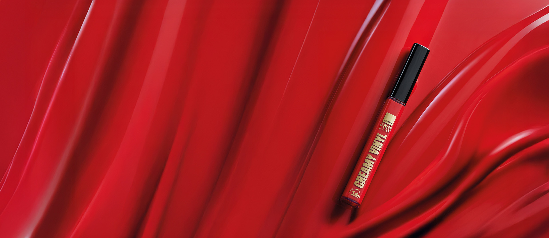 Batom Líquido Avon Power Stay Creamy Vinyl Vermelhaço com tampa preta. Ele está sobre um fundo líquido vermelho, imitando o próprio produto.