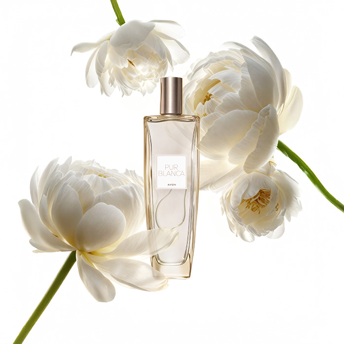 Frasco da fragrância Pur Blanca, rodeada de flores brancas, em fundo branco.