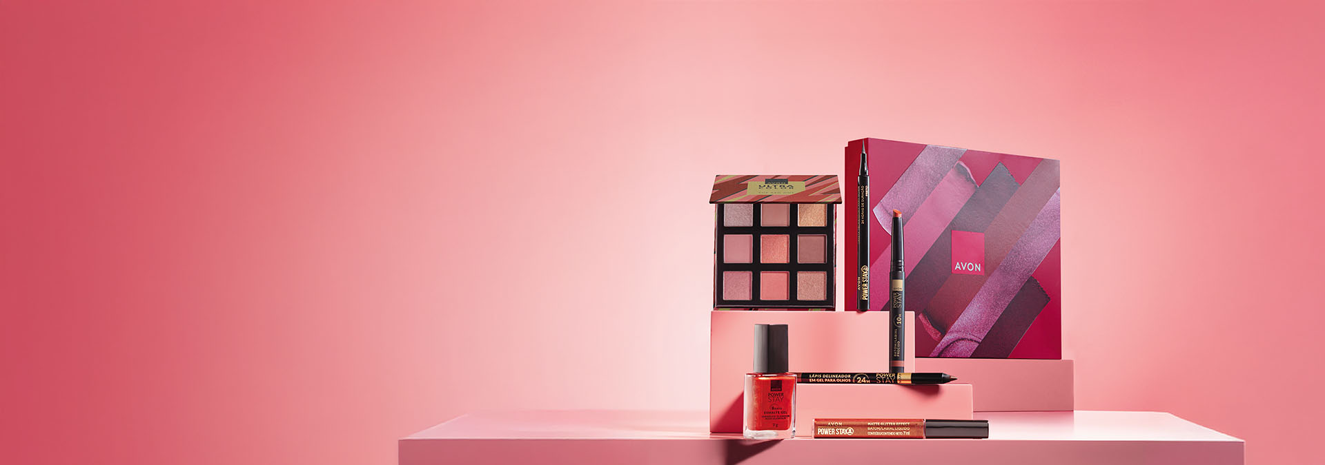 Banner com fundo rosa degradê. Elementos em plataformas geométricas destacam paleta de sombras, batom líquido, lápis delineador e esmalte. Texto: "Presentes Avon para unir laços e espalhar beleza."