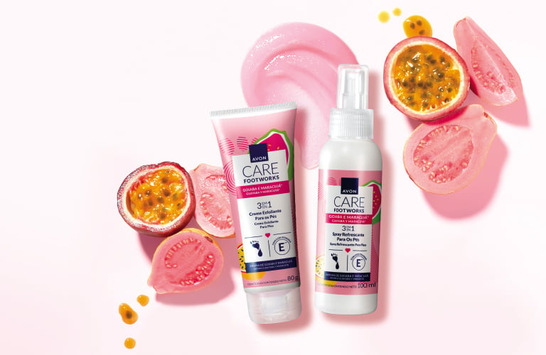 Duas embalagens brancas com detalhes em rosa e verde: um tubo de esfoliante corporal e um frasco de spray para os pés. Ao redor dos produtos, estão espalhadas metades de maracujá com sementes visíveis, pedaços de goiaba e amostras texturizadas dos cremes em tons de rosa.