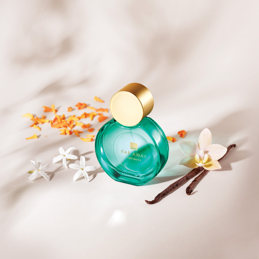 Frasco verde com tampa dourada de Far Away Infinity sobre bancada branca iluminada com ingredientes como flores brancas e amarelas e favo de baunilha.