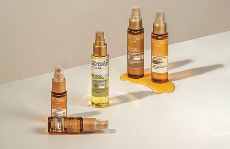 Cinco óleos capilares para umectação capilar da Avon colocados verticalmente em fundo neutro. Um dos frascos de 30ml está caído.