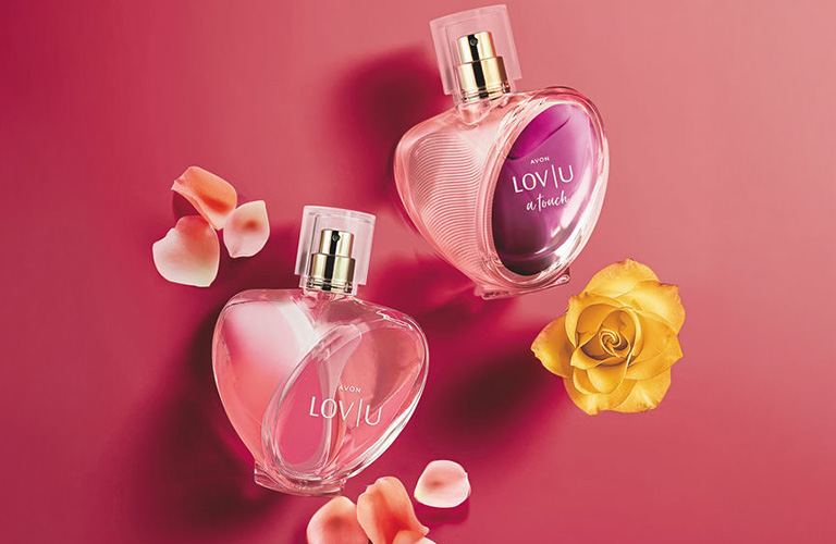 Perfumes Avon LOV U em formato de coração e frasco rosa. Ao lado, rosas amarelas, brancas e laranjas representando as notas de perfume