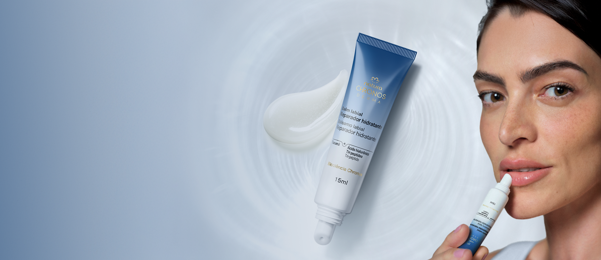 Mulher branca de cabelo escuro aplica o Balm Labial Reparador Hidratante Chronos Derma nos lábios. Ao lado, sobre fundo azul com ondulações, bisnaga azul e branca com textura do produto em destaque.
