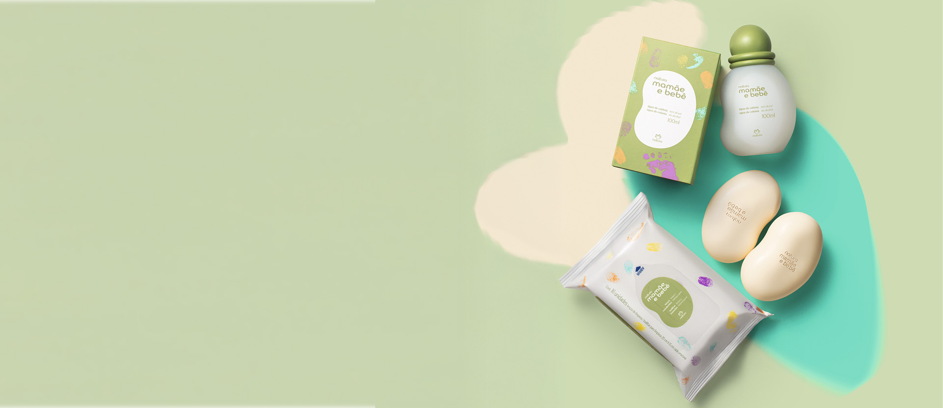 Produtos Mamãe e Bebê sobre fundo verde-claro e amarelo suave: água de colônia, 2 sabonetes bege e lenços umedecidos. Embalagens em branco e verde, com pequenos desenhos de mãos e pés coloridos.