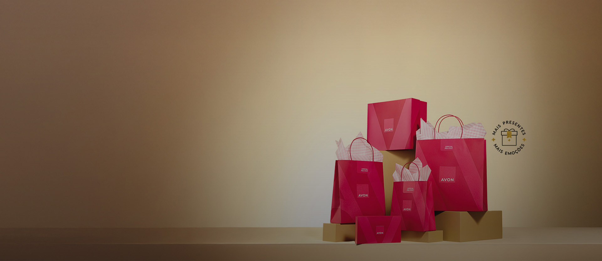 Banner com com fundo bege degradê e elementos que incluem caixas e sacolas rosas da Avon sobre bases douradas. Texto: Embalagens traduzem amor e cuidado. Presenteie com Avon.