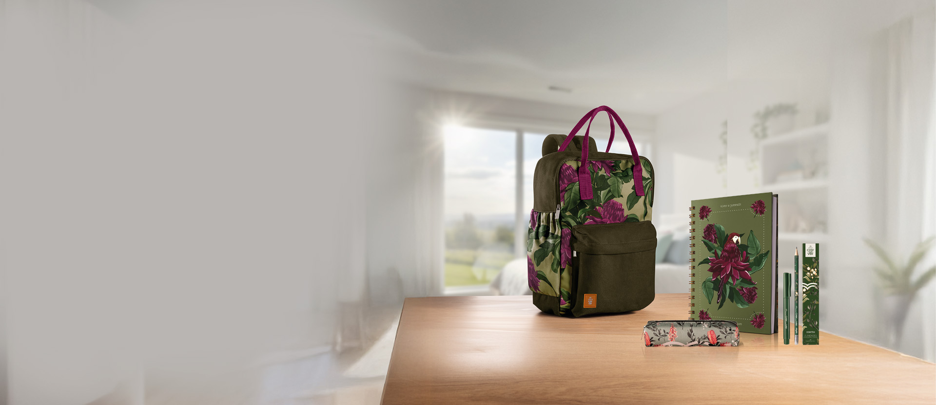 Produtos Crer Para Ver sobre mesa de madeira: mochila verde com estampa floral roxa, caderno verde com estampa de flores e pássaro roxo, estojo verde com estampa floral e caixa com lápis e caneta verdes.
