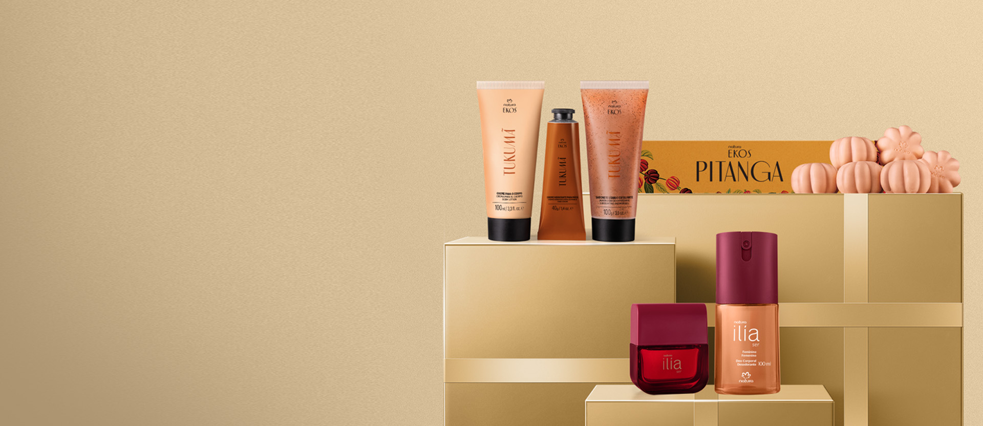 Produtos sobre caixas douradas: bisnagas laranja de creme corporal, creme de mãos e esfoliante Ekos Tukumã; caixa laranja com sabonetes Ekos Pitanga; frascos vermelhos do deo parfum e deo corporal Ilía Ser.