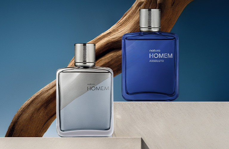 Foto con fondo azul. Dos frascos de perfume Natura Homem y Natura Homem Absoluto sobre bloques de concreto con madera al fondo.