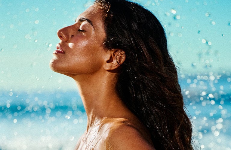 Foto con fondo desenfocado de una mujer de perfil con un traje de baño blanco en el mar