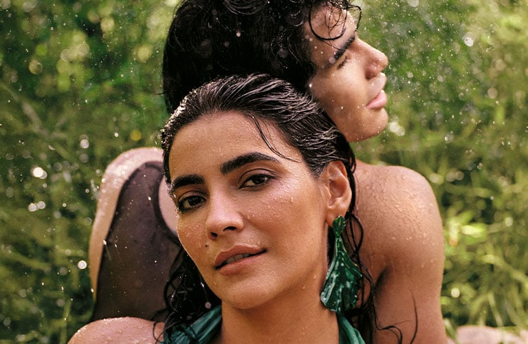 Foto de mujer y hombre en un entorno verde con gotas de agua. La mujer en primer plano lleva un vestido