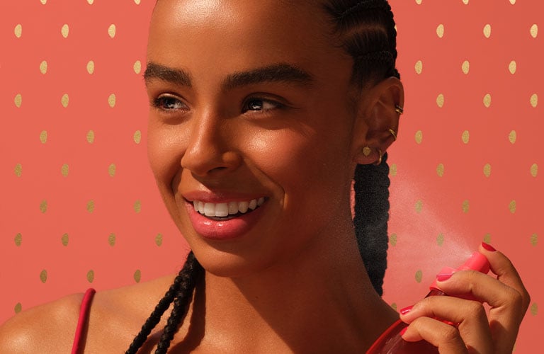 Foto de una persona con trenzas usando un spray para el cabello. Fondo coral con puntos dorados. Elementos: vestido rojo y frasco rojo con atomizador que libera niebla.