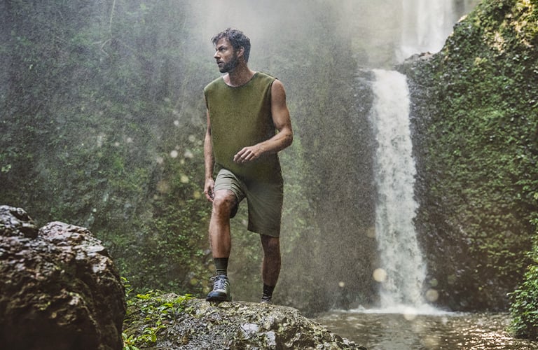 Hombre haciendo trekking en un ambiente natural con una cascada de fondo.