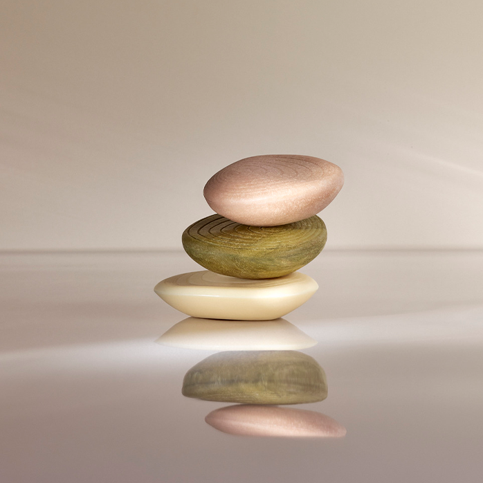 Tres productos de la línea Natura Biōme equilibrados en una superficie. Las barras son de colores: rosa, verde y blanco.