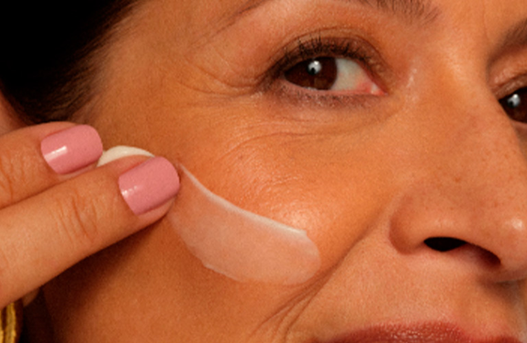 Foto de mujer aplicando una crema facial sobre la mejilla.