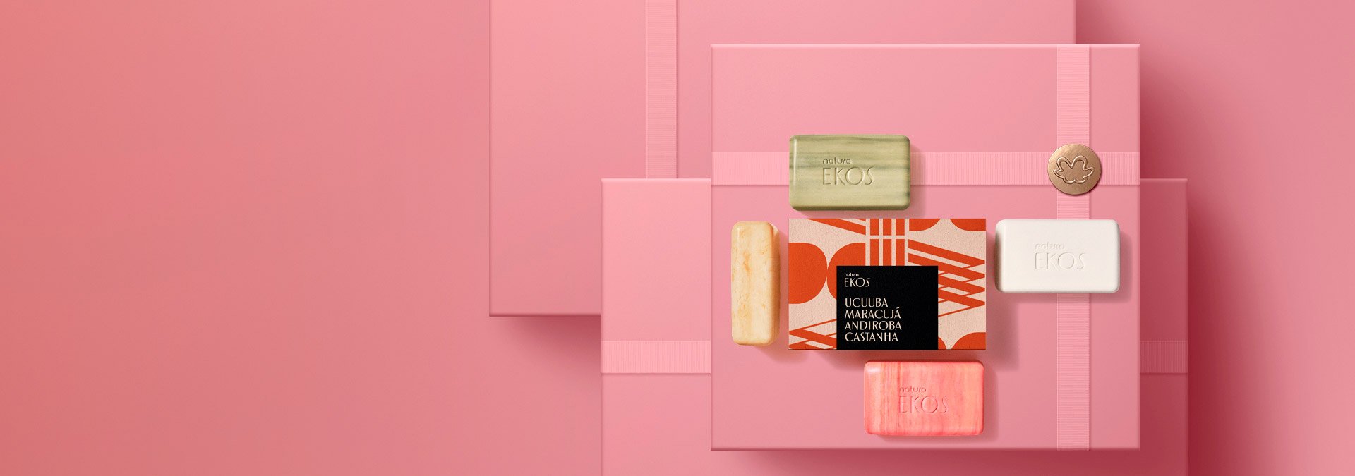 Sobre un fondo rosa con cajas de regalos, una caja de jabones Ekos con los jabones esparcidos fuera de la caja.