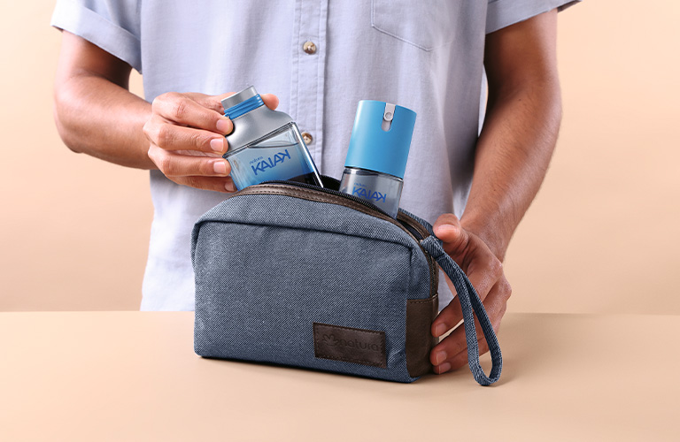 Foto con fondo beige. Manos masculinas sacando un frasco de perfume Kaiak de un neceser azul sobre una mesa.