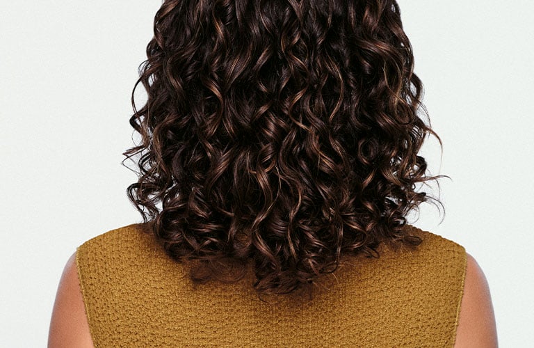 Close up mujer de espaldas con blusa verde y rizos sueltos.