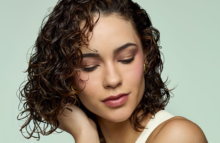 Foto de una mujer con cabello rizado corto, los ojos cerra