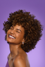Foto de mulher de cabelos curtos e cacheados sorrindo, em fundo roxo.