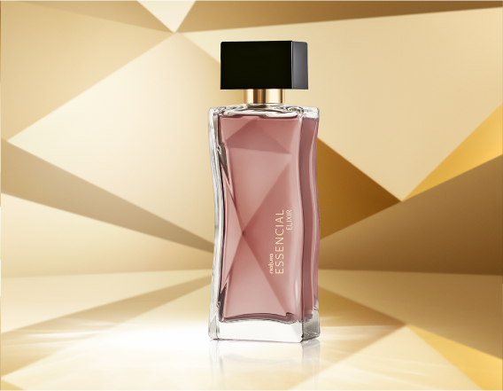 Frasco de Essencial Elixir Feminino, em tons de rosê e tampa preta, aparece em destaque no centro da tela sobre fundo multifacetado dourado, fazendo alusão ao design do frasco de Essencial.