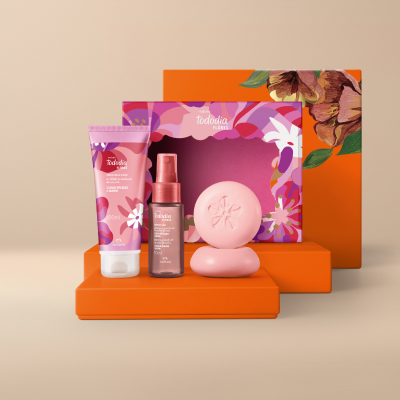 Presente Natura Tododia Flores Essenciais, contendo 1 Body Splash, 1 Creme Desodorante Nutritivo para o Corpo e 2 Sabonetes em Barra flor de pêssego e jasmim. Os itens estão sobre caixas de presentes laranja.