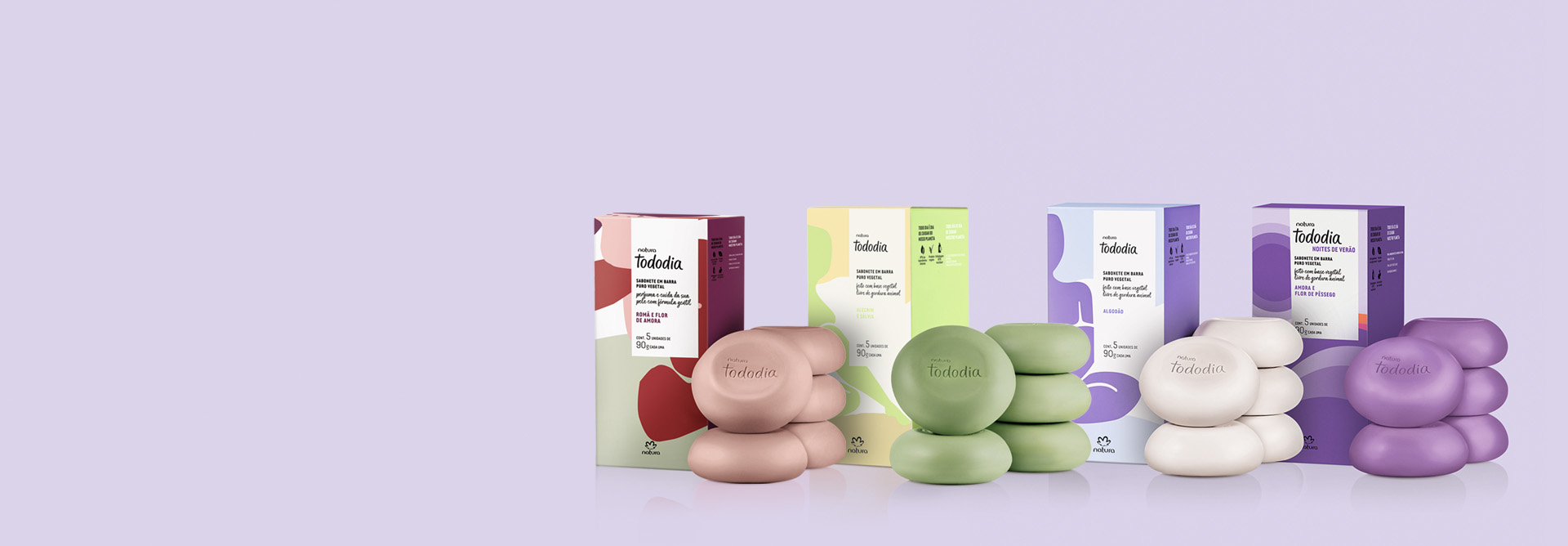Kit de Sabonetes em Barra Tododia com quatro caixas, nas fragrâncias Romã e Flor de Aroma, Alecrim e Sálvia, Algodão e Amora e Flor de Pêssego aparecem ao lado de suas caixas sobre fundo lilás.