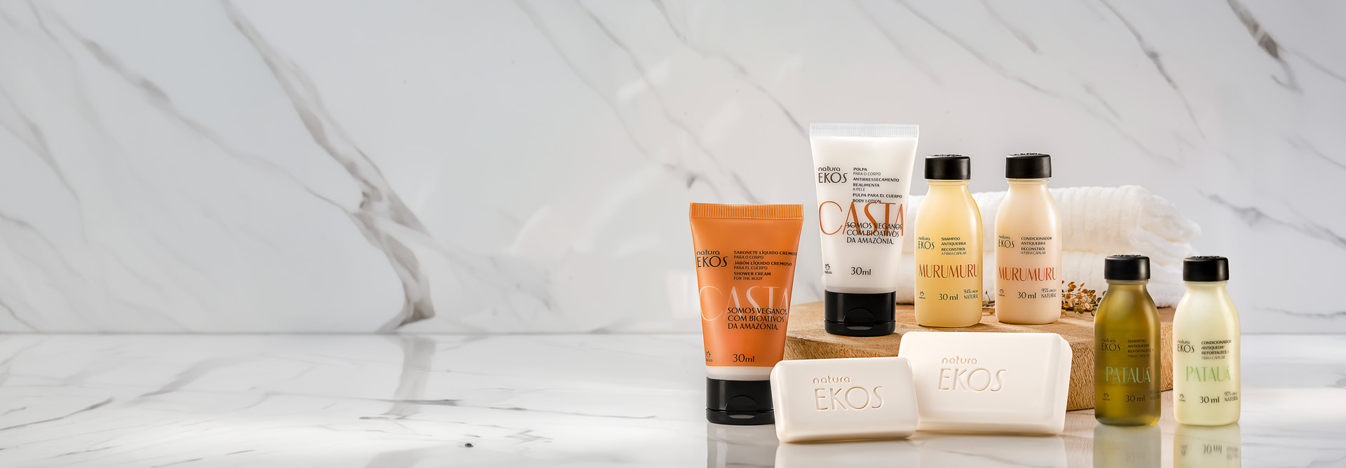 Kit de amenidades Natura Ekos com sabonetes, cremes e óleos das linhas Castanha, Murumuru e Patauá, organizados sobre base de madeira com toalhas e flores secas ao fundo.