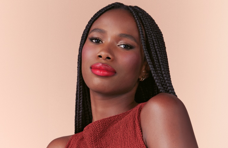 Mulher usando tranças e batom vermelho posando para a foto com um ar sério